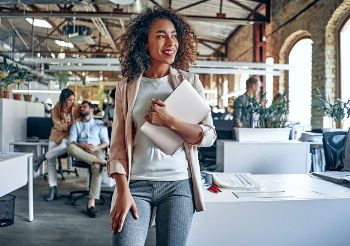 Women smiling in office setting holding laptop