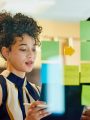 Woman putting post-it notes on glass during brainstorm session at work.