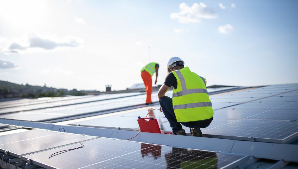 Man in safety vest working on installing solar panels in field.