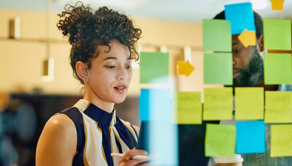 Woman putting post-it notes on glass during brainstorm session at work.