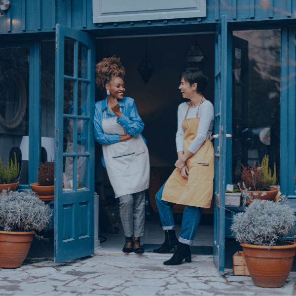 Two women wearing aprons standing in a door frame laughing